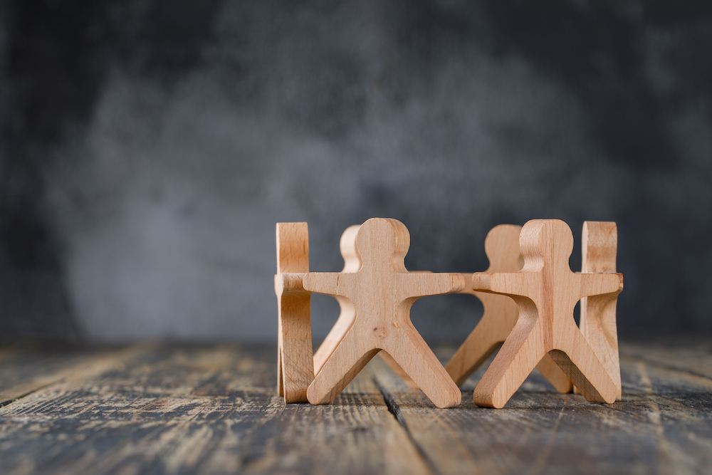 Business success and teamwork concept with wooden figures of people on wooden and foggy background side view.