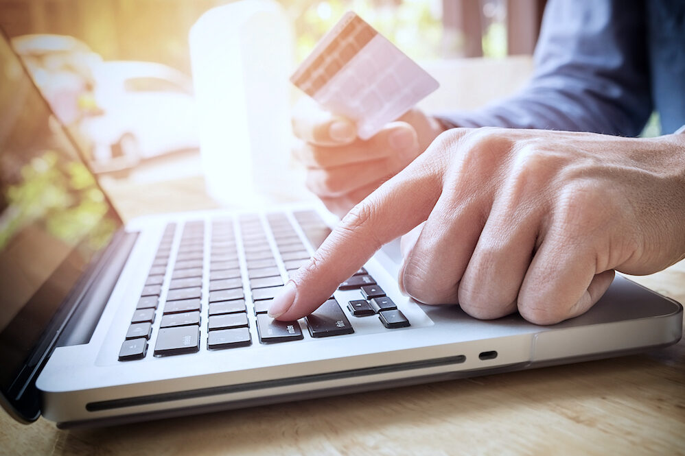 Man holding credit card in hand and entering security code using laptop keyboard