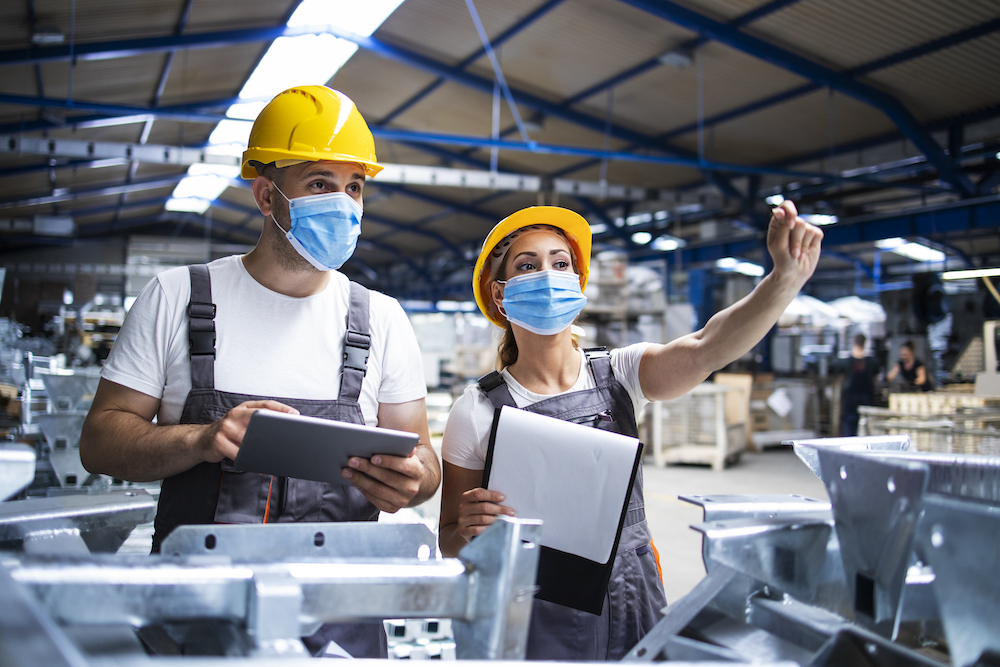 Factory workers with face masks protected against corona virus doing quality control of production in factory.